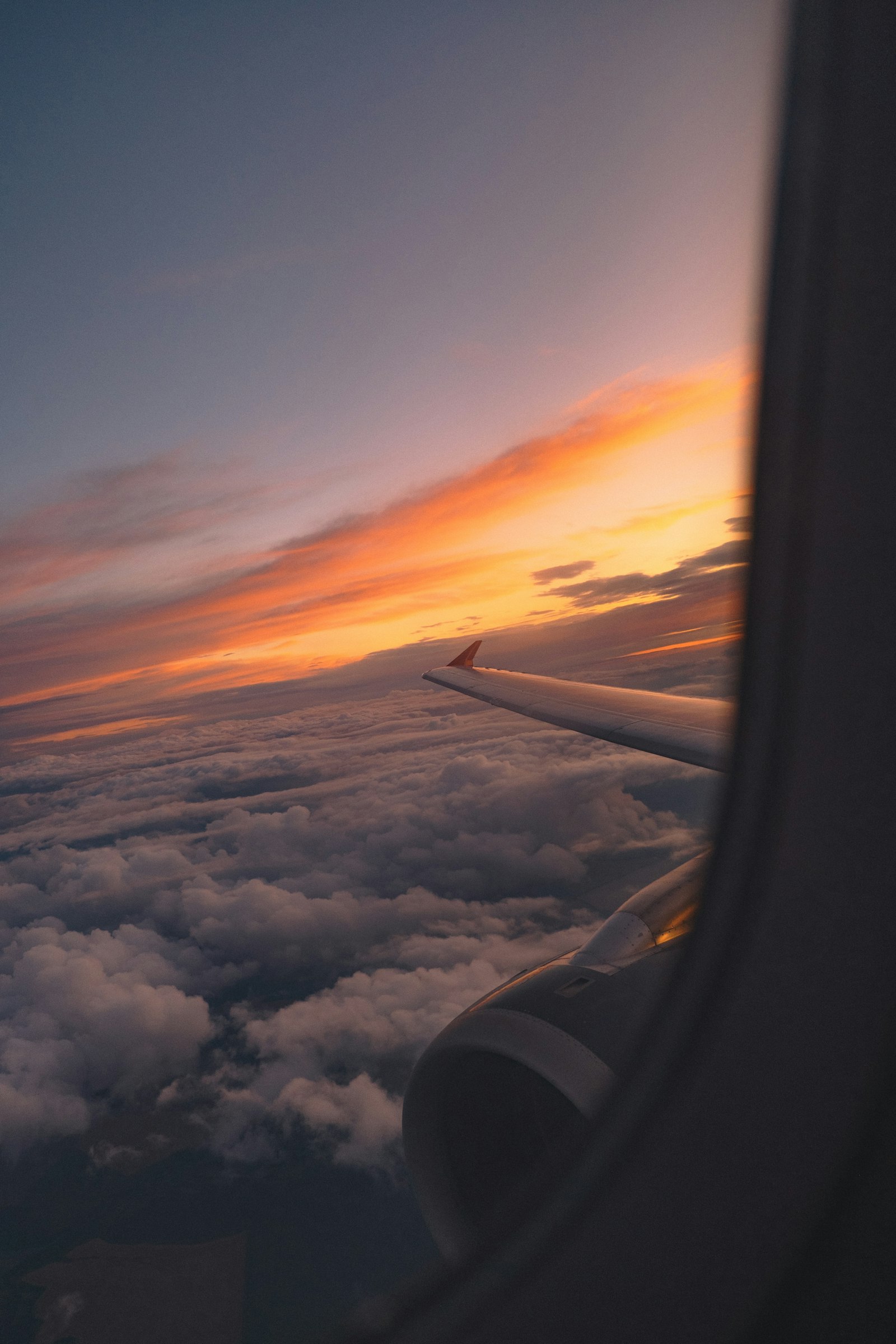 Airplane wing and engine silhouetted against a sunset sky above clouds