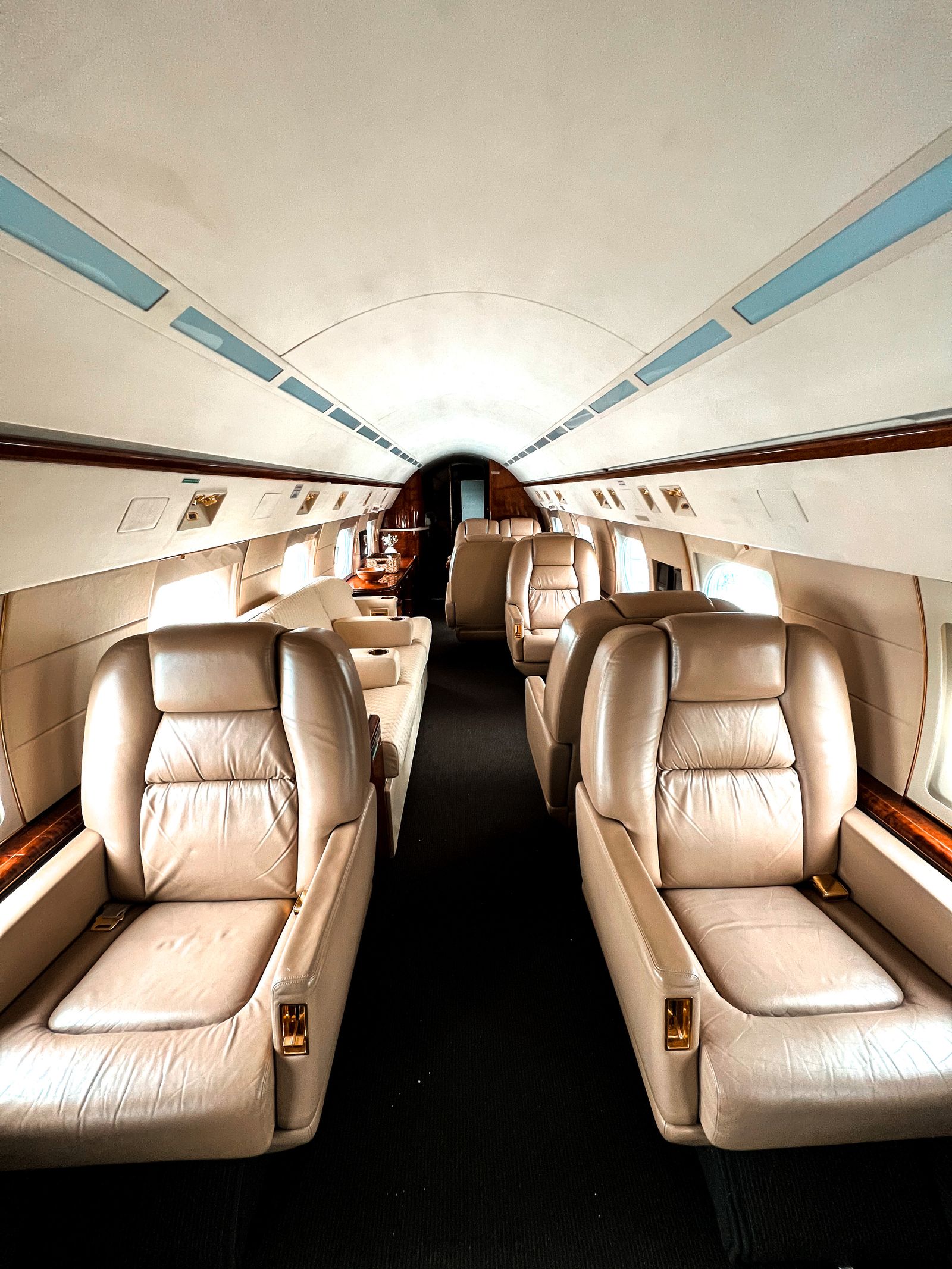 The empty cabin of a private jet, cream leather seats down a symmetric aisle with wood trim.