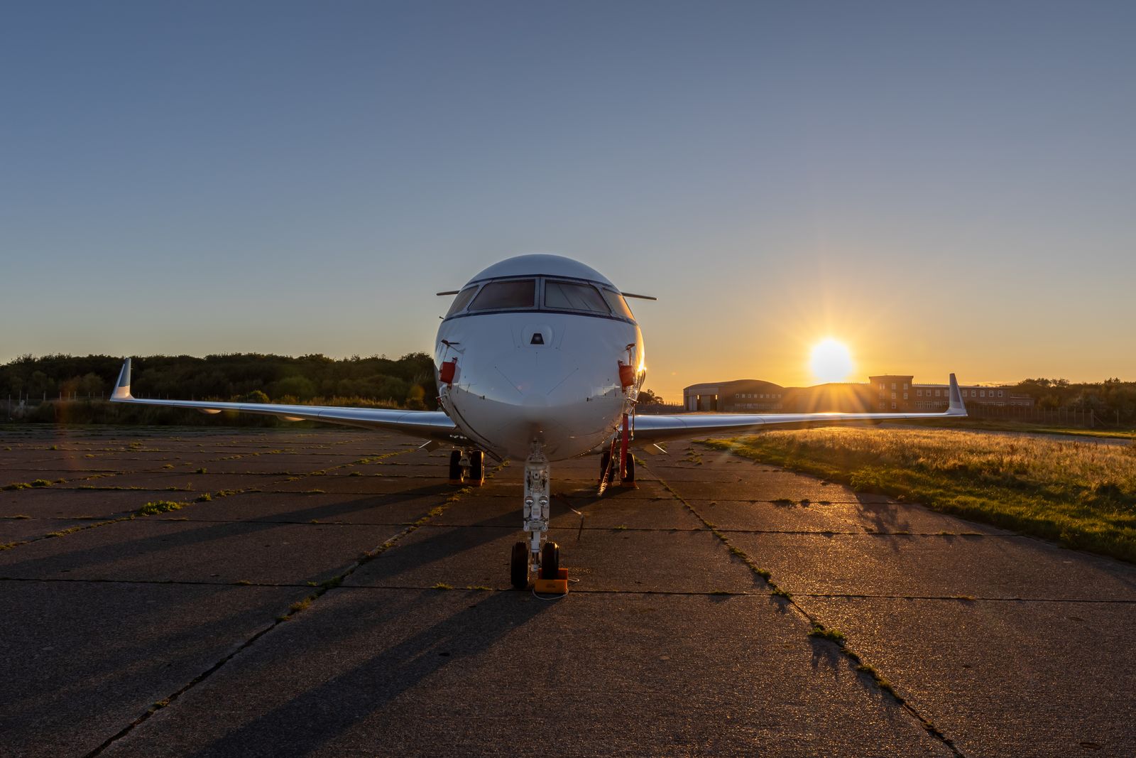 A business jet facing down a runway at sunset, the sun flaring low behind it.
