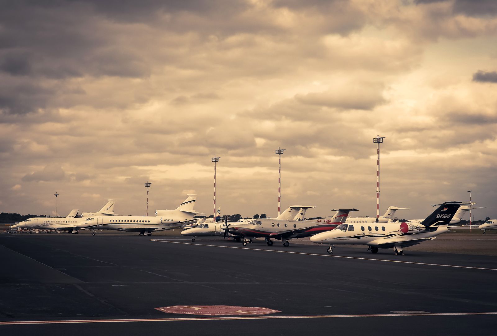 Five business jets and turboprops parked in a line on an airport ramp under a heavy overcast sky