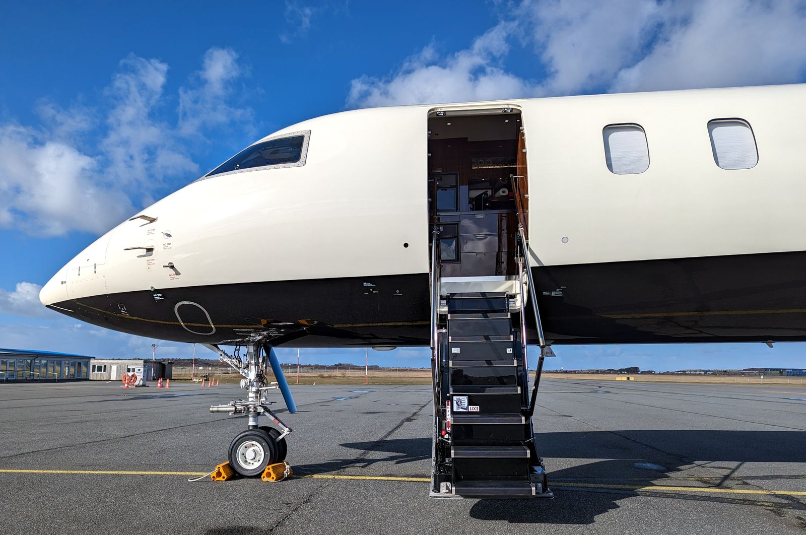 A white business jet parked on a ramp with its cabin door open and airstairs lowered, under a blue sky with scattered cloud