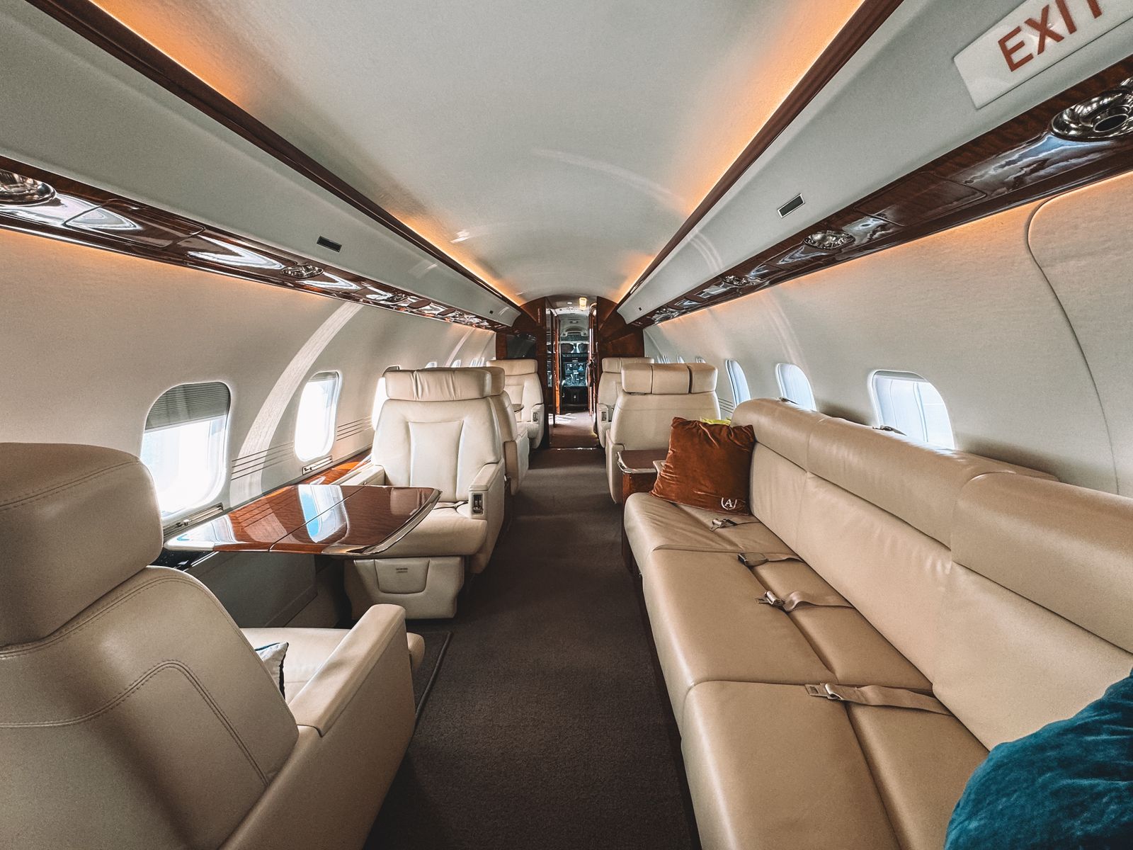The empty cabin of a business jet, with cream leather seats, a polished wood table and an illuminated exit sign